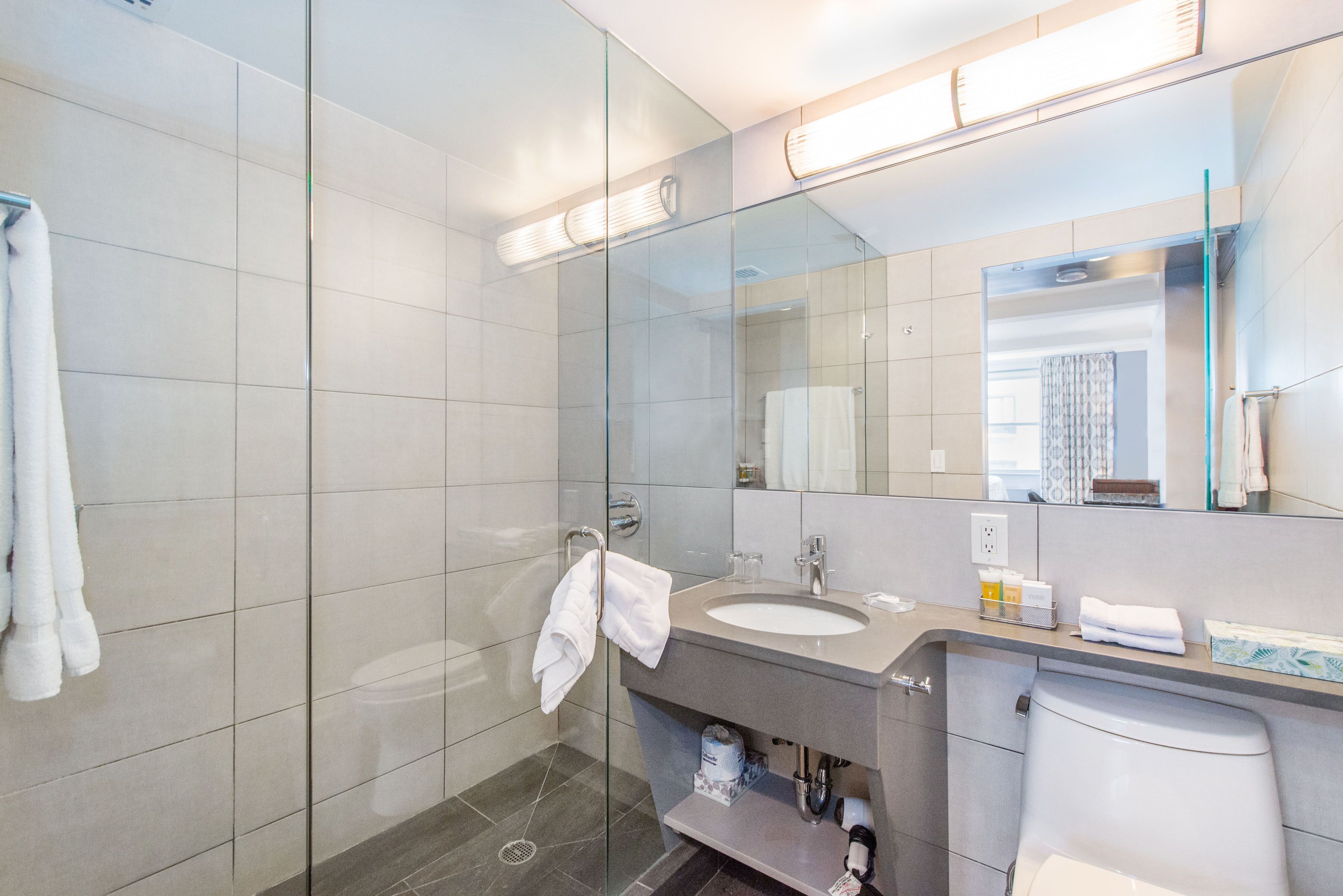 A modern bathroom with a glass shower enclosure, a sink with a mirror above it, and a toilet.