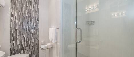 A modern bathroom with a glass-enclosed shower, a toilet, and a sink.