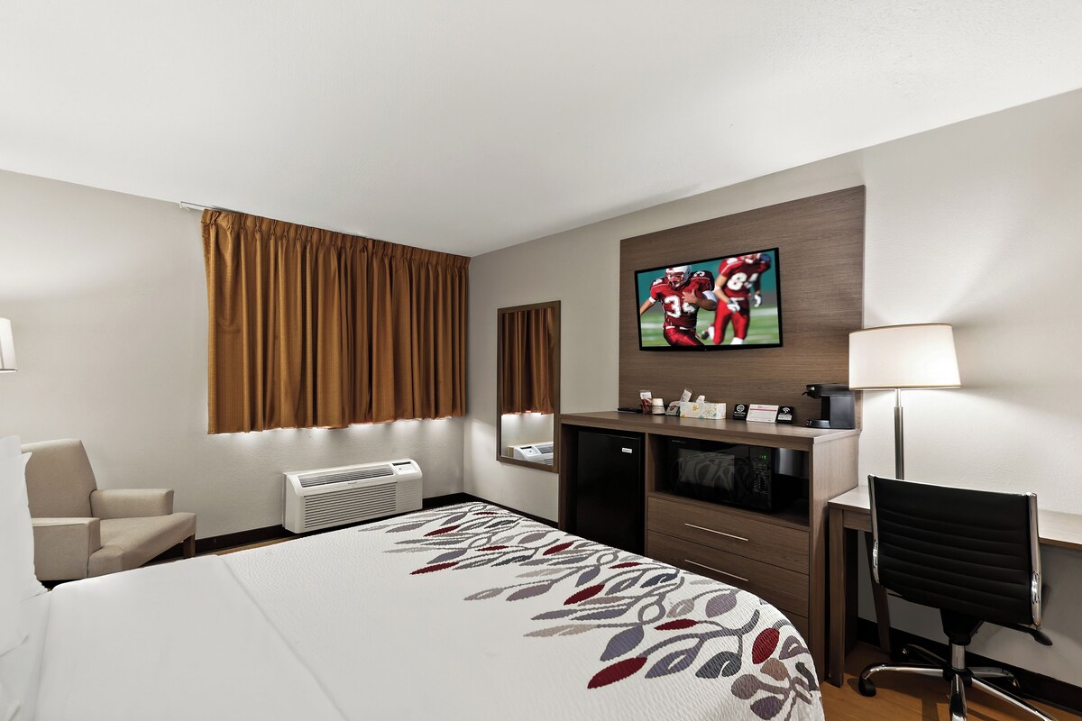 A hotel room with a bed, a desk, a chair, a TV, and a minibar.