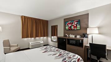 Habitación de hotel con cama, escritorio, silla, televisor y minibar.