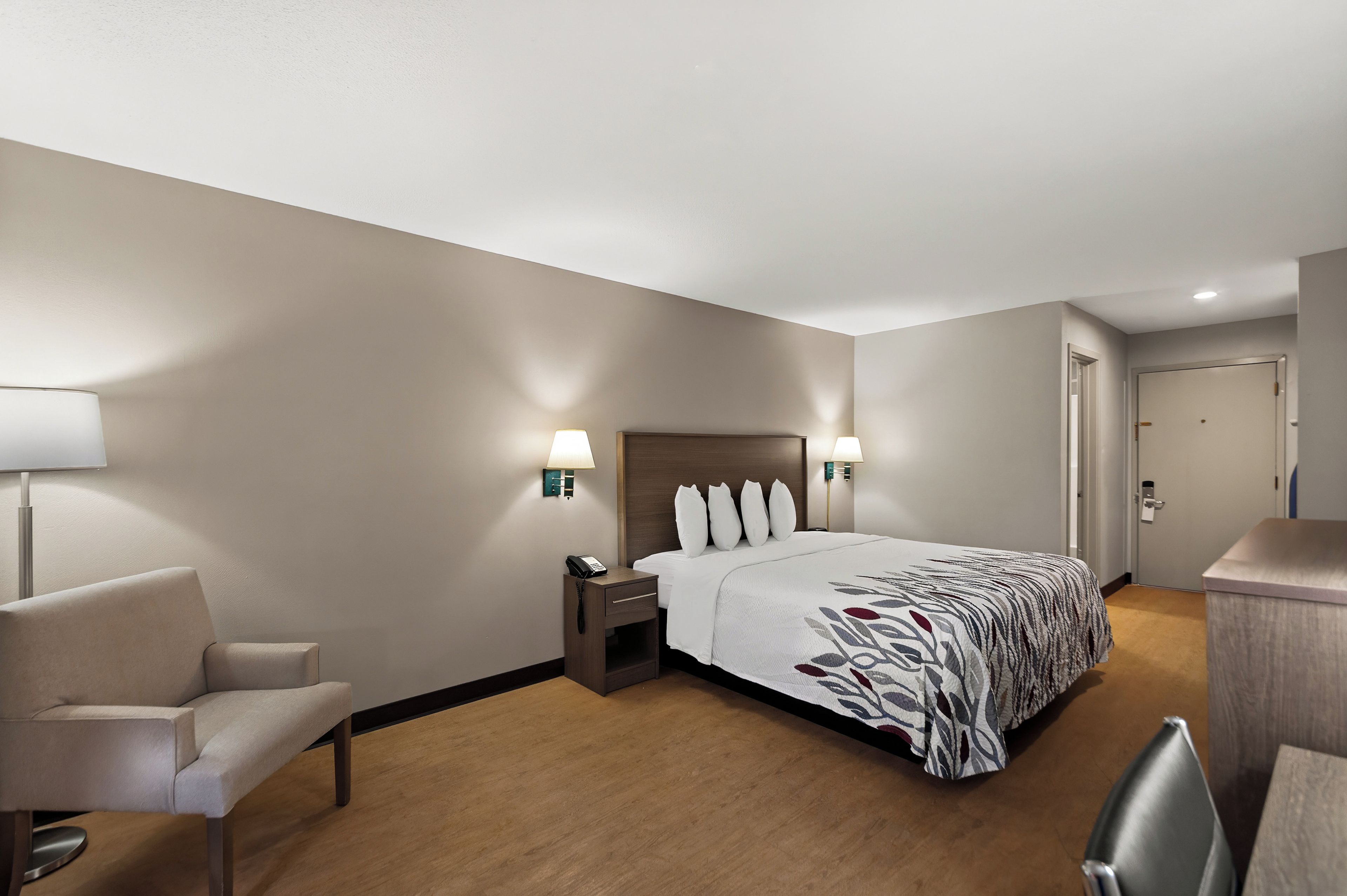 A hotel room with a bed, bedside lamps, a chair, a desk, and a door.