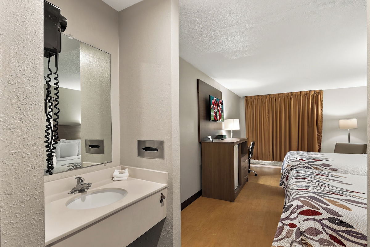 A hotel room with a bathroom, a bed, a desk, and a television.