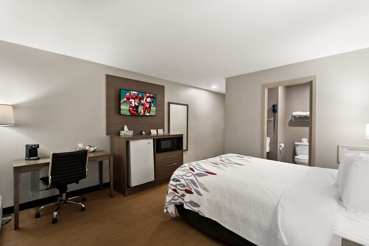 Ein Hotelzimmer mit Bett, Schreibtisch, Stuhl, Fernseher und einer kleinen Küchenzeile.