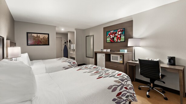 Habitación de hotel con dos camas, un escritorio, una silla, un televisor y un microondas.