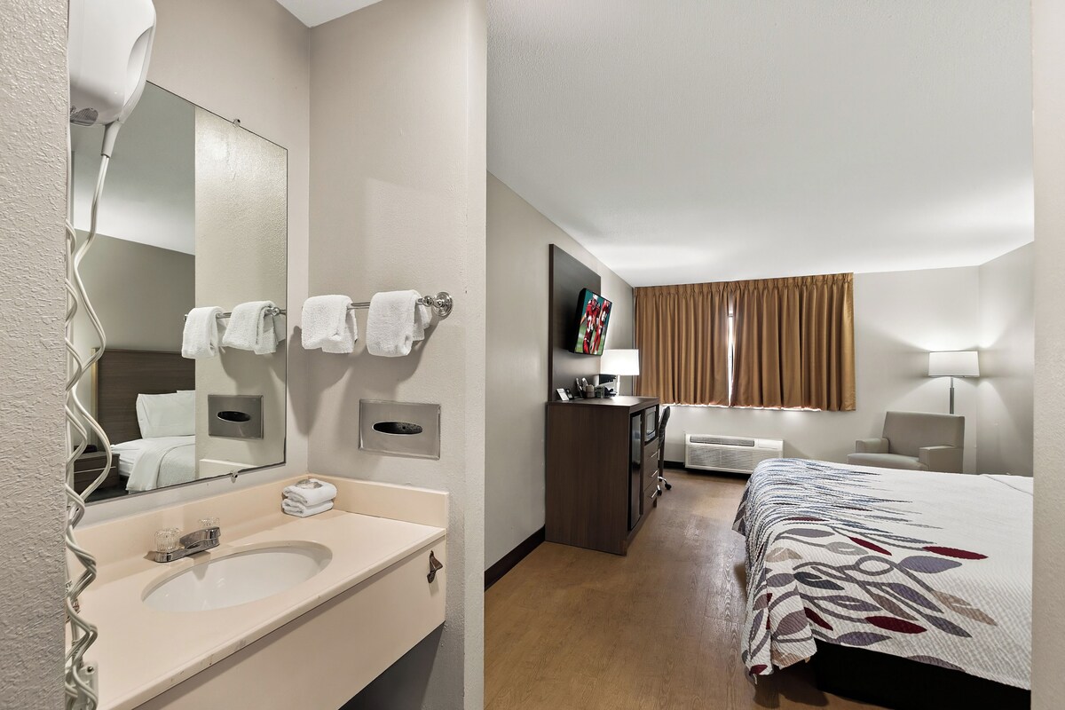 A hotel room with a bathroom, a bed, a desk, and a TV.