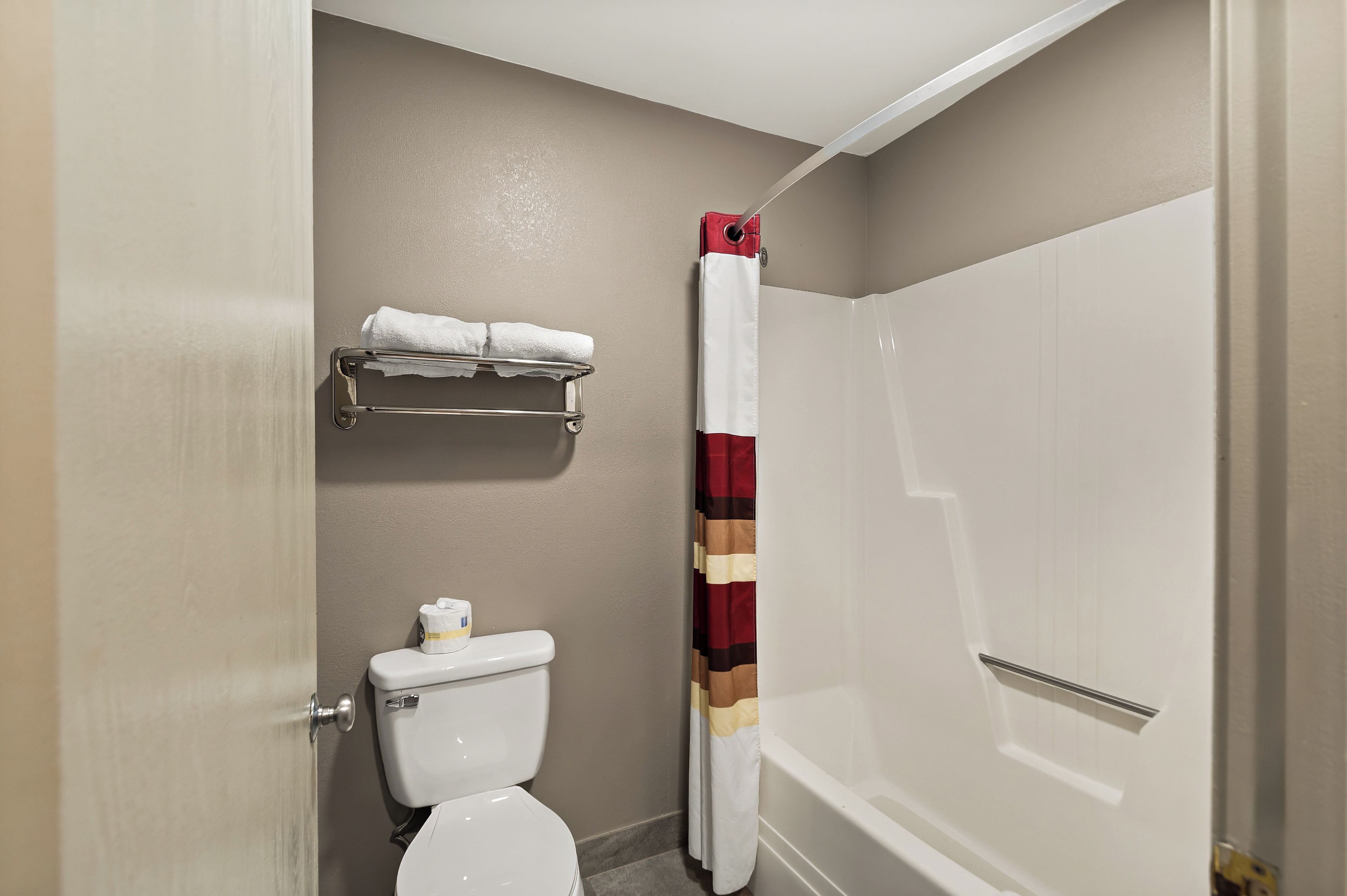 A bathroom with a toilet, a towel rack with a white towel, a striped shower curtain, and a bathtub.