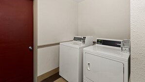 Un lavadero con dos lavadoras y secadoras blancas, una puerta roja y una pared blanca.