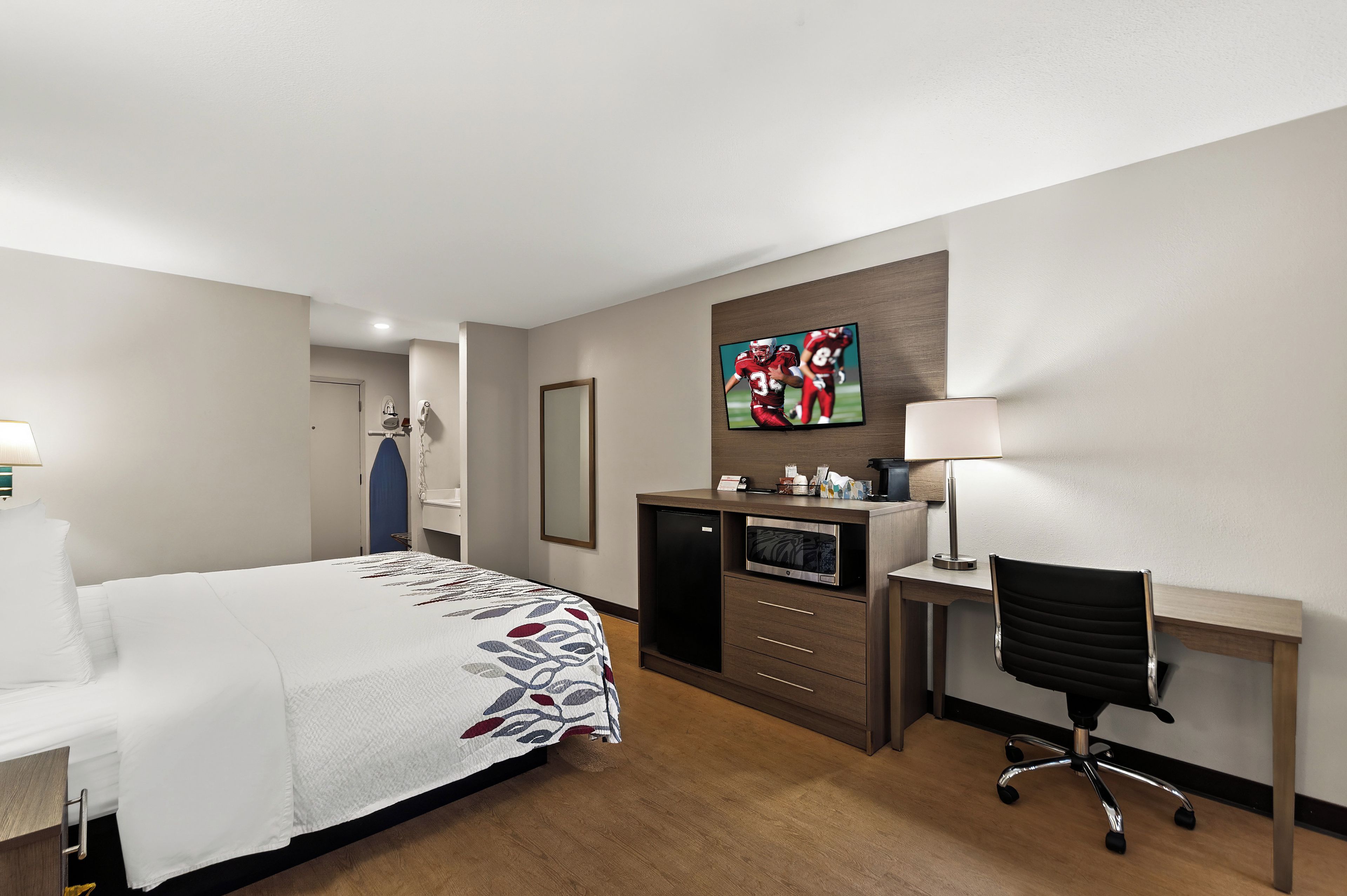 A hotel room with a bed, desk, chair, TV, and a mirror.