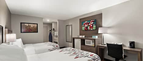 Habitación de hotel con dos camas, un escritorio con computadora, una silla, televisor y refrigerador.
