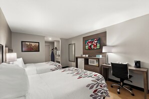 A hotel room with two beds, a desk with a computer, a chair, a TV, and a refrigerator.