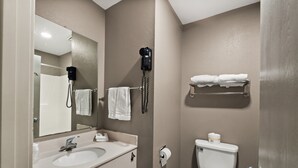 Un baño con lavamanos, espejo, toallero, inodoro y un secador de pelo fijado en la pared.
