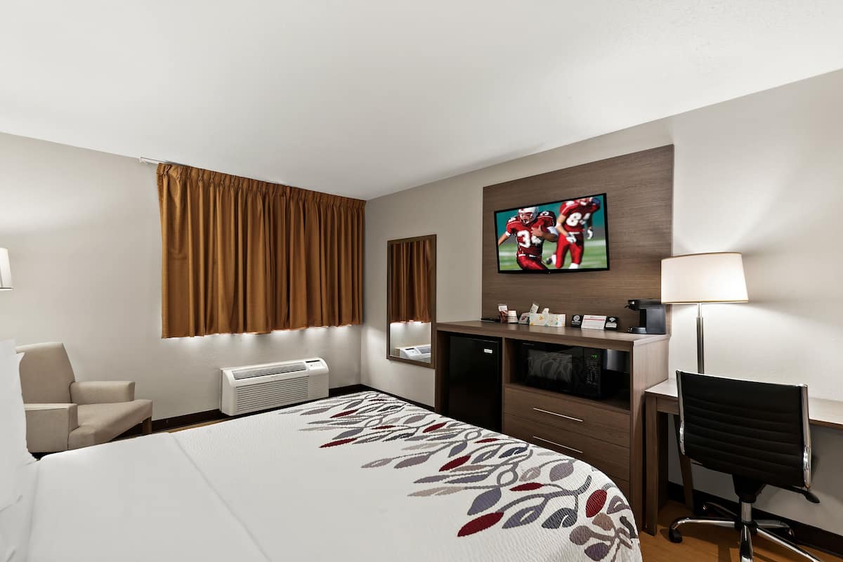 Ein Hotelzimmer mit einem Bett, einem Schreibtisch, einem Sessel, einem Fernseher und einem Spiegel.
