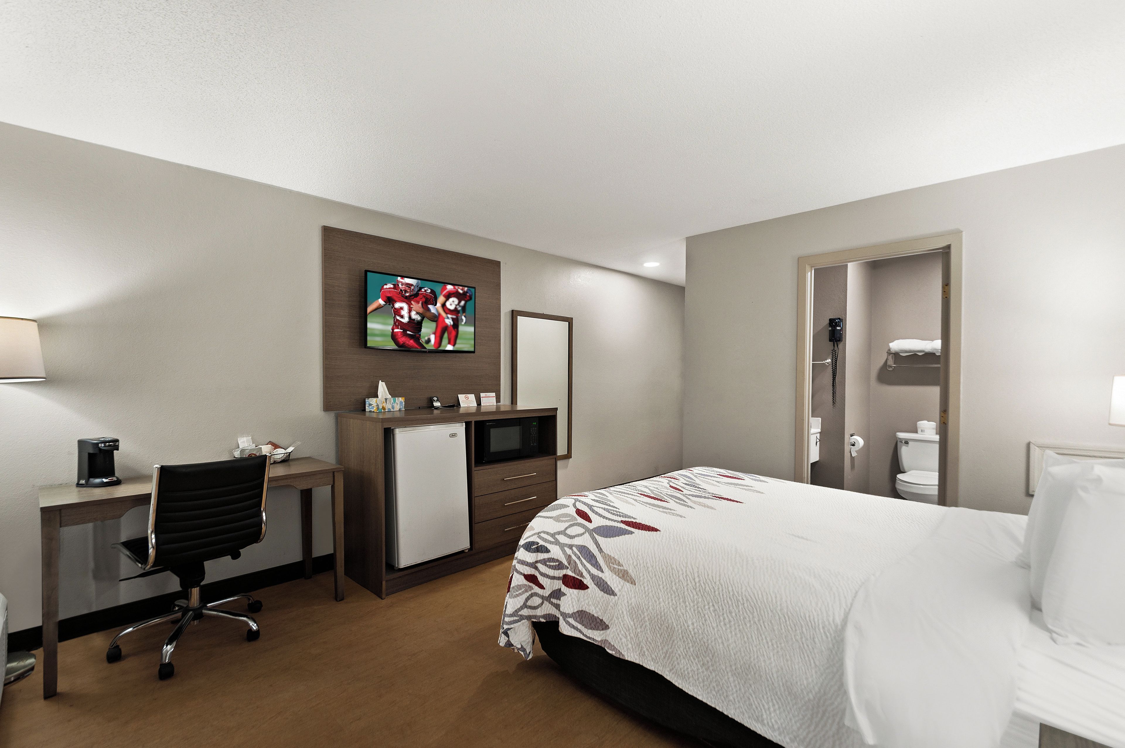 A hotel room with a bed, desk, chair, and a television mounted on the wall.