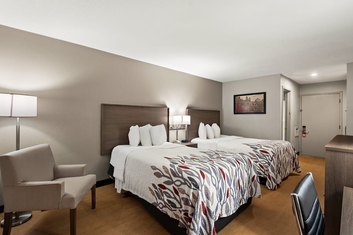 Ein Hotelzimmer mit einem großen Bett, zwei Nachttischen, einem Sessel, einem Schreibtisch und einer Lampe.