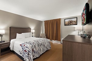 Habitación de hotel con cama, mesitas de noche, escritorio, silla, televisor y ventana con cortinas.