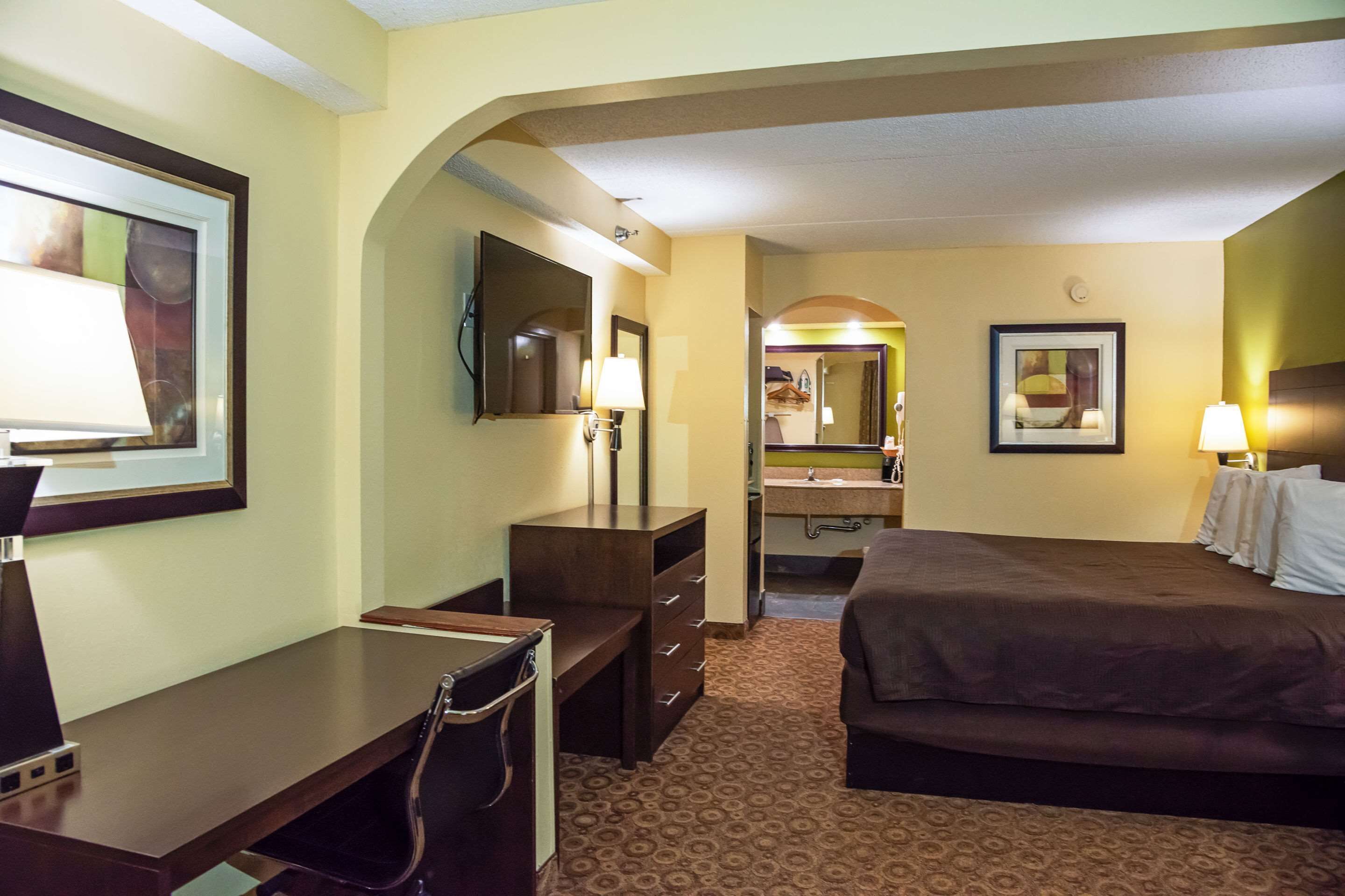 A hotel room with a bed, desk, chair, and a bathroom with a sink and mirror.