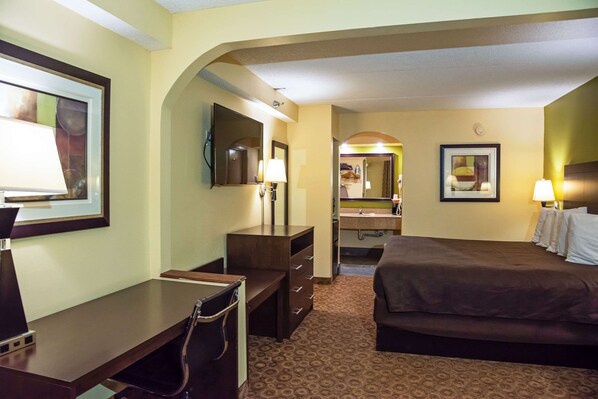 A hotel room with a bed, desk, chair, and a bathroom with a sink and mirror.