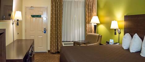 Een hotelkamer met een bed, een stoel, een bureau, een lamp en een deur.