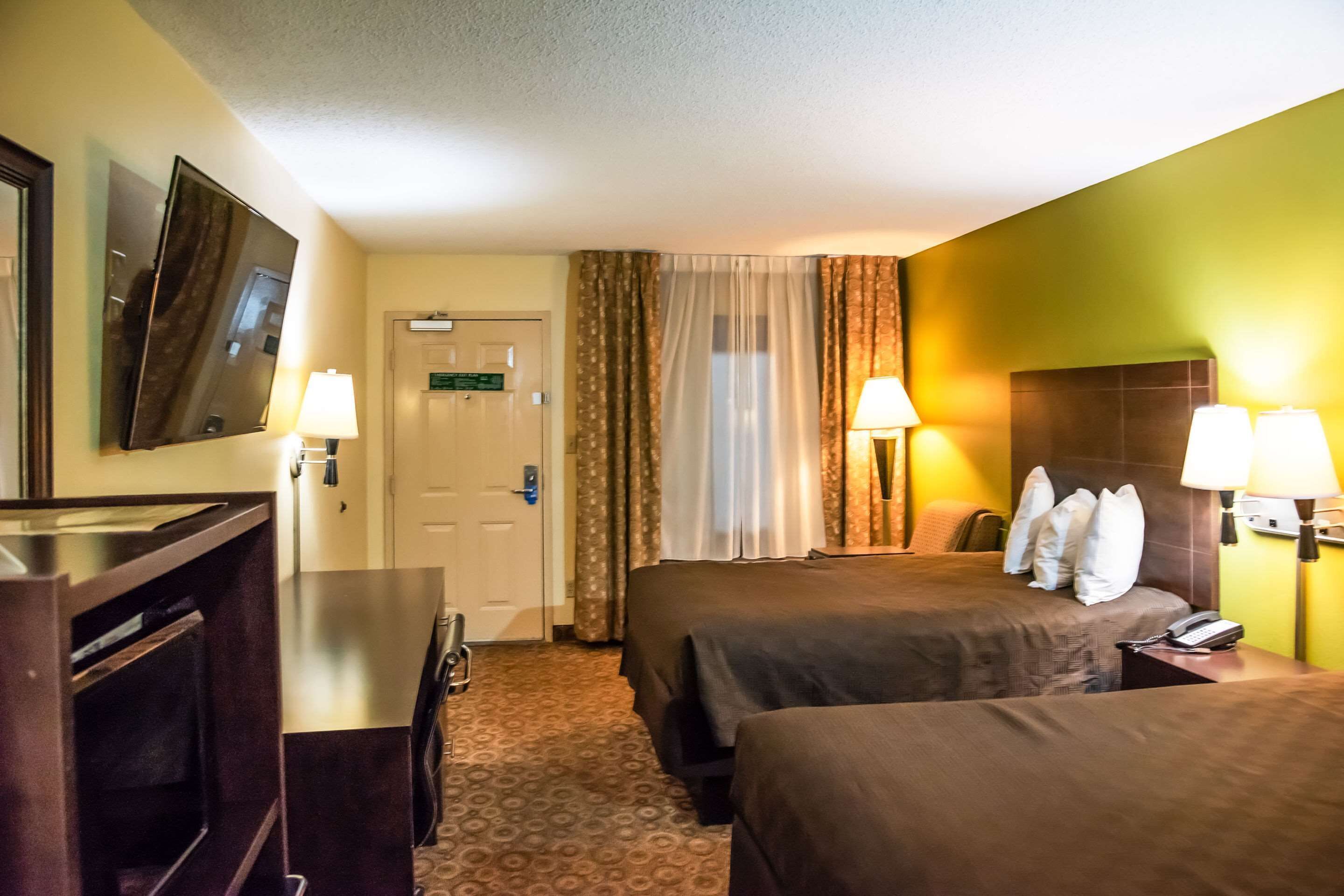 Habitación de hotel con dos camas, un escritorio, un televisor y una puerta.