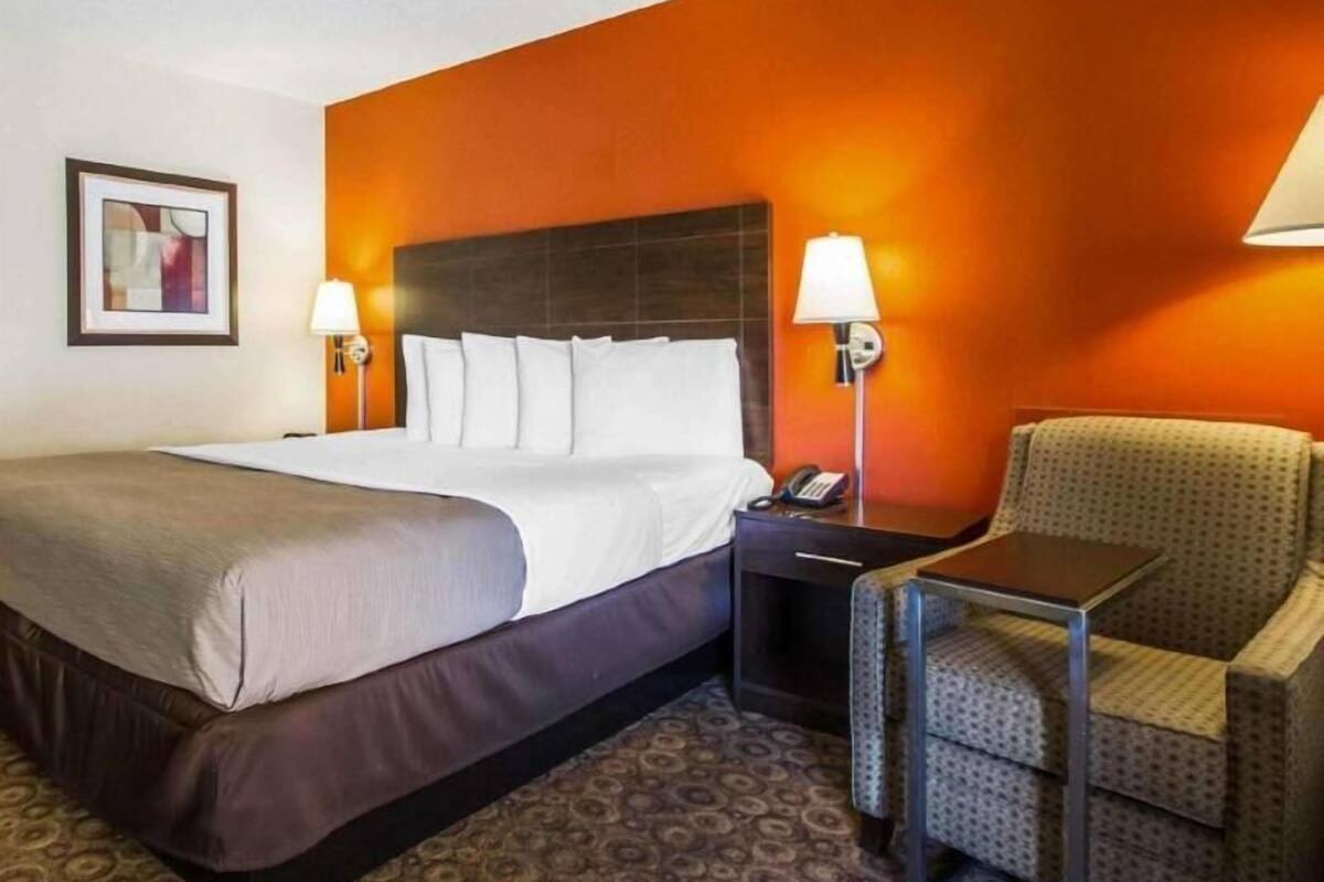 A hotel room with a large bed, two bedside lamps, a chair, a nightstand, and a framed picture on the wall.