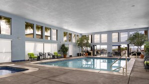 Une piscine intérieure à l’eau d’un bleu cristallin, entourée de chaises longues et de plantes en pot.