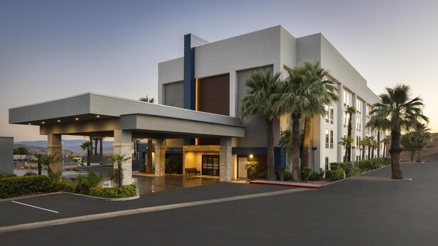 Un hôtel moderne doté d’une entrée couverte, de palmiers et d’un parking.