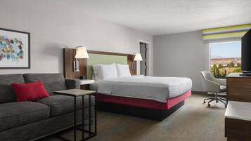 A hotel room with a bed, a desk, a chair, and a sofa.