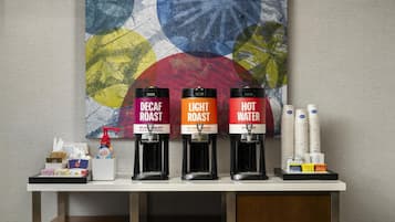 A coffee station with three dispensers labeled 'Decaf Roast,' 'Light Roast,' and 'Hot Water.' There are also stacks of disposable cups and a box of tissues.