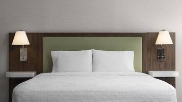 Una cama bien tendida con un edredón blanco texturizado, dos lámparas de noche y un cabecero de madera con un panel verde.