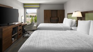 Une chambre d’hôtel avec deux lits, une télévision, un bureau avec une chaise et une vue sur l’extérieur.