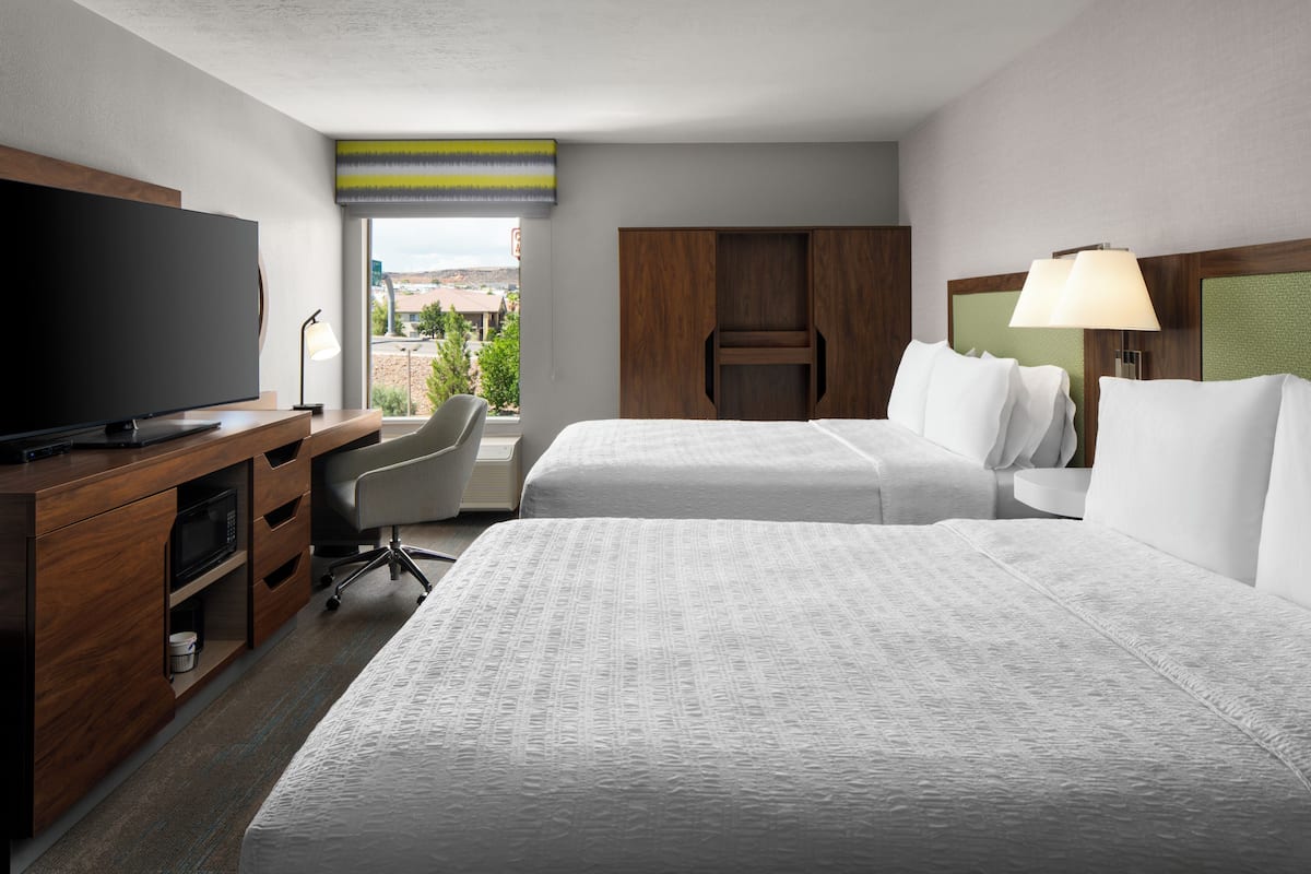 A hotel room with a TV, two beds, a desk, and a chair.