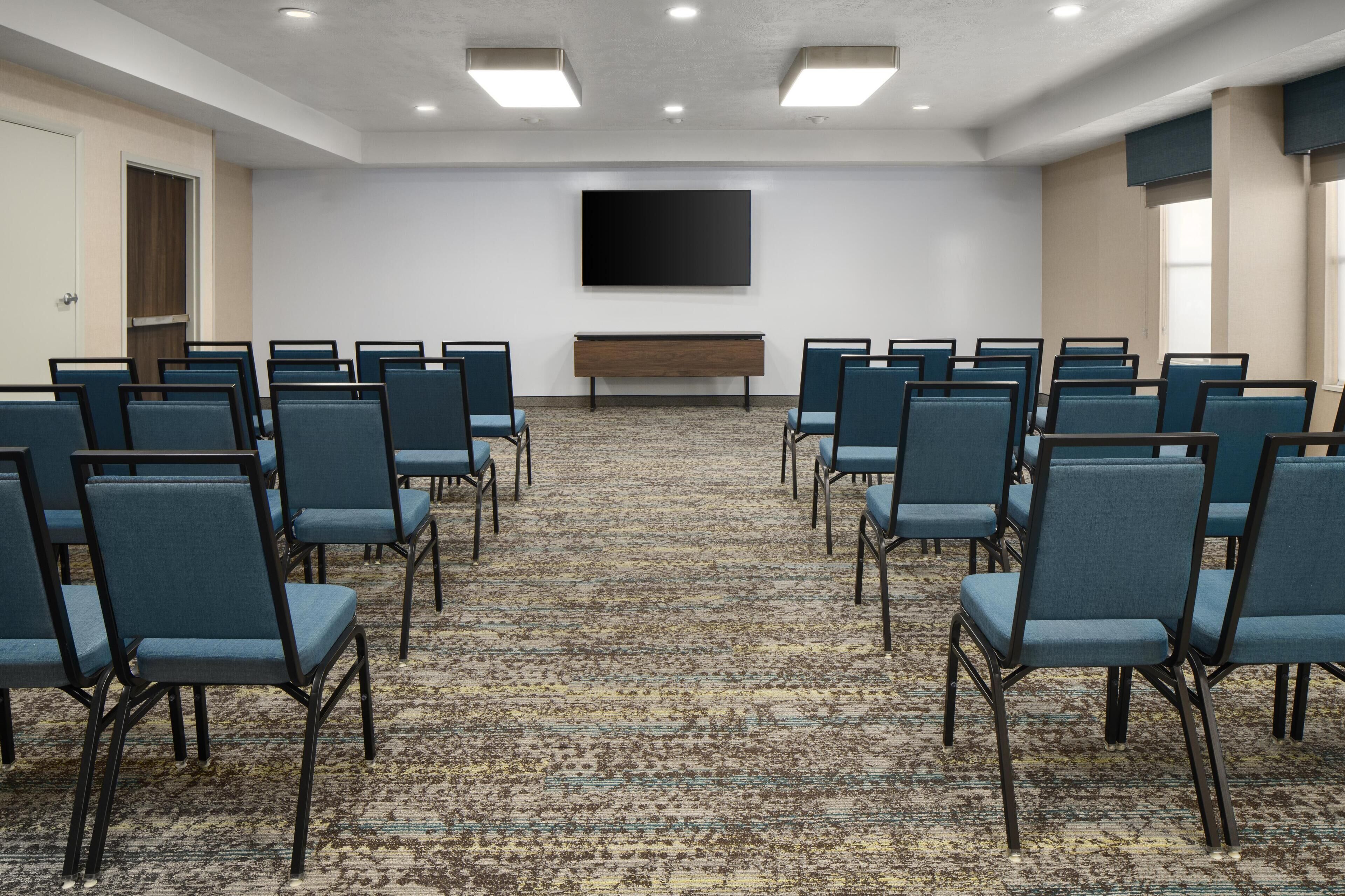 A conference room with rows of chairs, a large flat-screen TV, and a carpeted floor.
