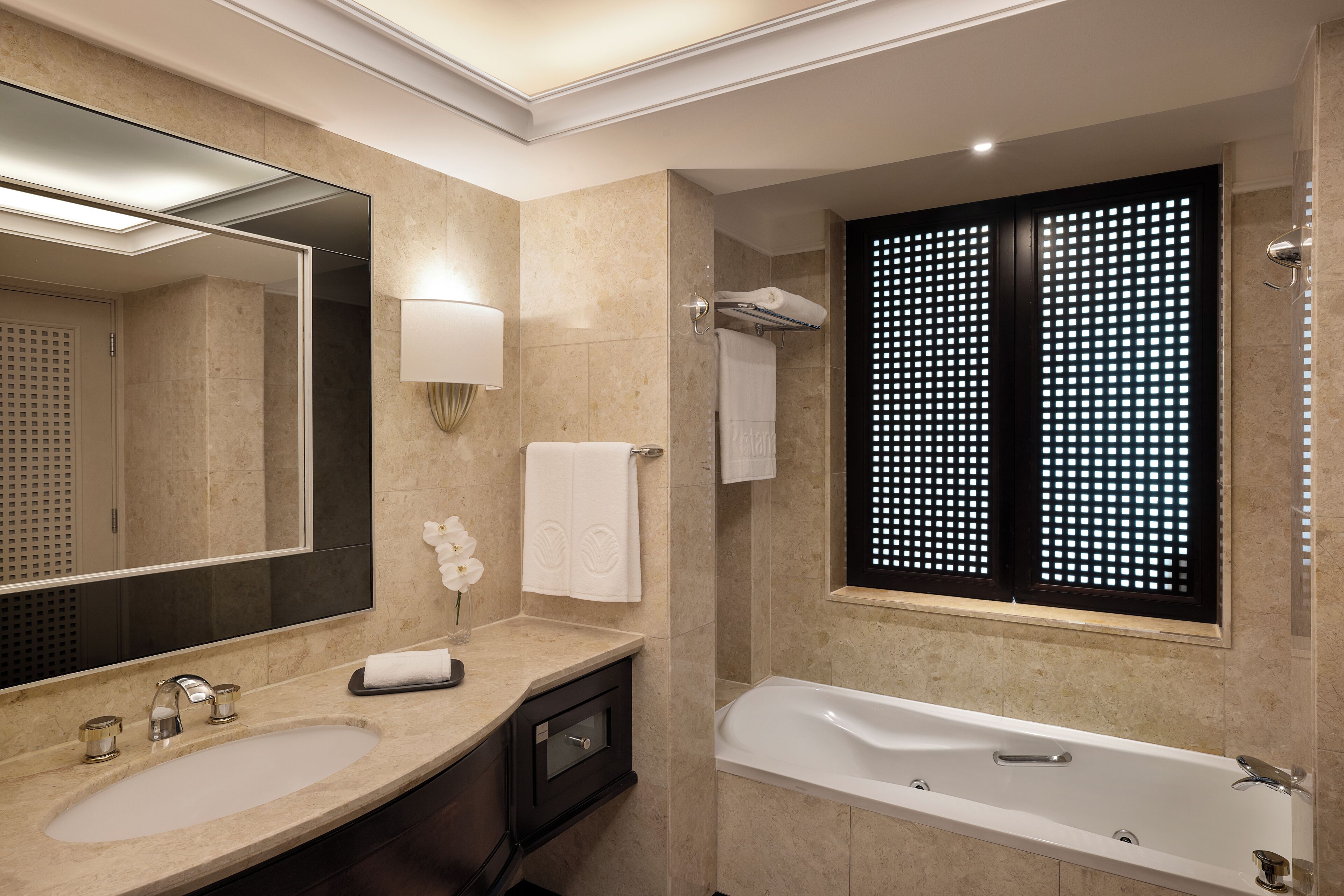Une salle de bain moderne avec un grand miroir, un lavabo, une baignoire et une fenêtre agrémentée d’un paravent décoratif.