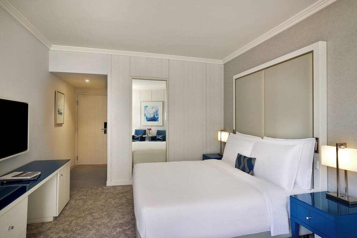 A hotel room with a large bed, a desk with a flat-screen TV, a mirror, and a nightstand with lamps.