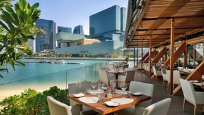 A restaurant with outdoor seating overlooking a marina and city skyline. - Beach Rotana (Abu Dhabi)