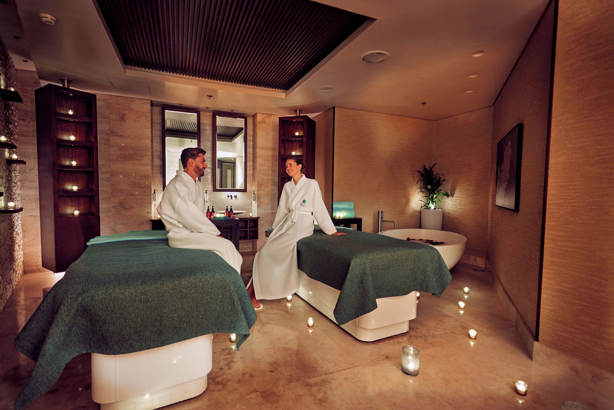 A spa room with two massage tables, a reception desk, and a mirror.