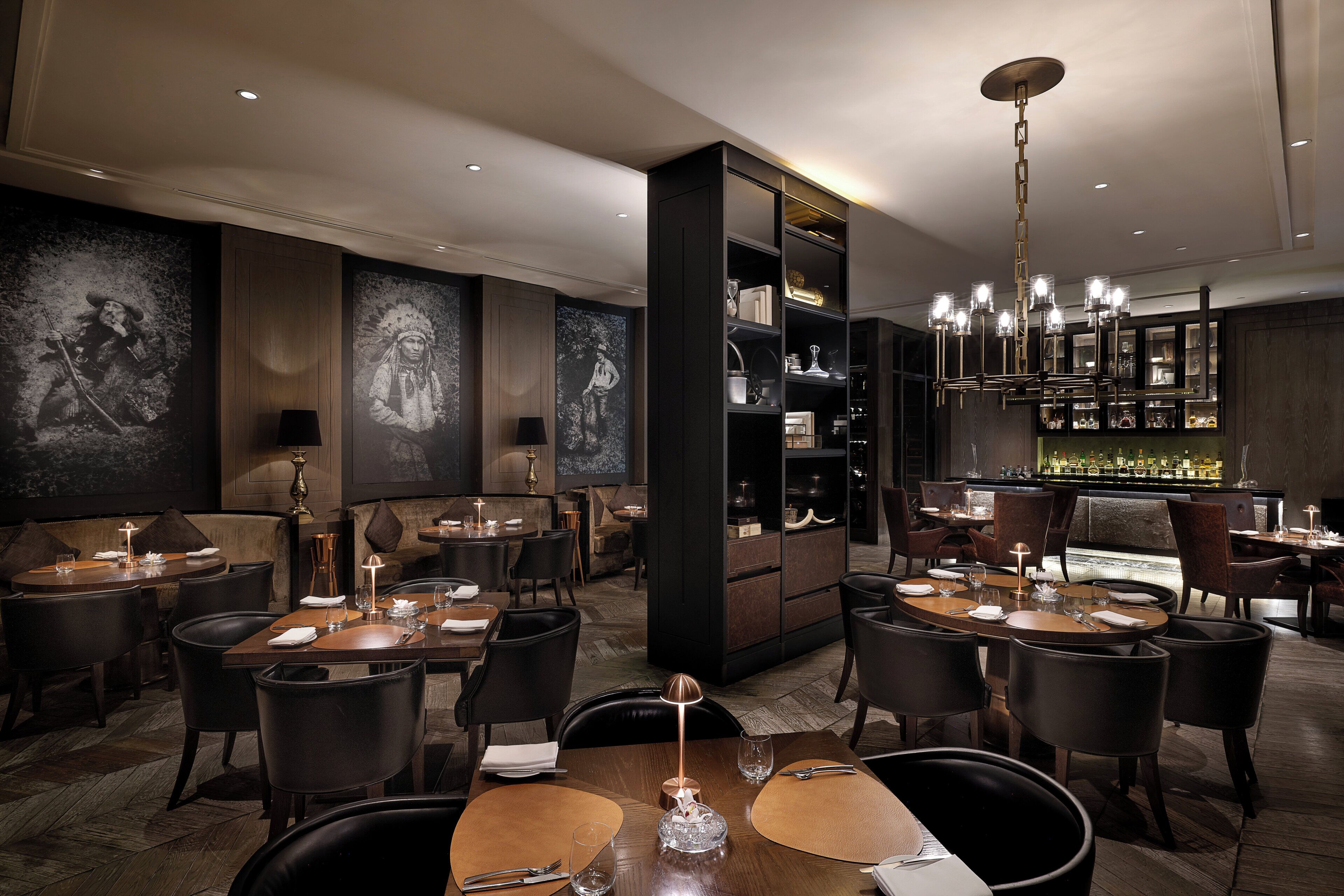 A restaurant with multiple tables, dark wood furniture, and a bar area with a well-lit ambiance.