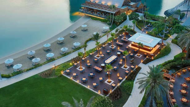 An aerial view of a resort with a pool, outdoor seating areas, and a building with a sloped roof. - Beach Rotana (Abu Dhabi)