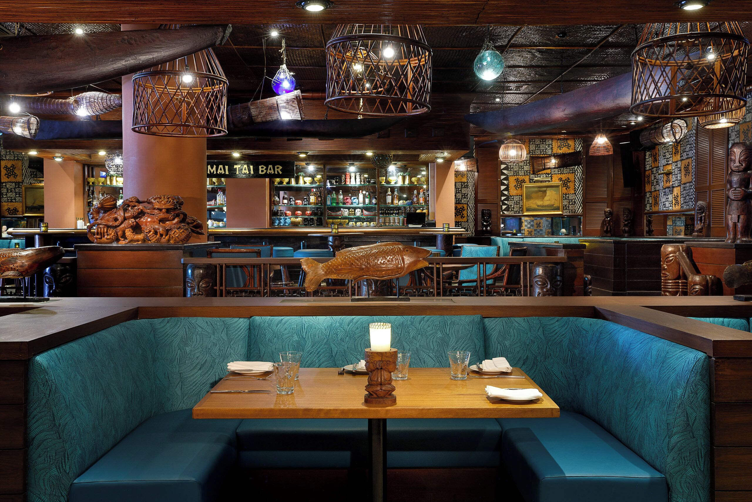Un restaurante con zona de bar, asientos tapizados en color aguamarina y decoración de madera.