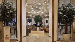 A spacious lobby with a central tree, elegant chandeliers, and a seating area. - Beach Rotana (Abu Dhabi)
