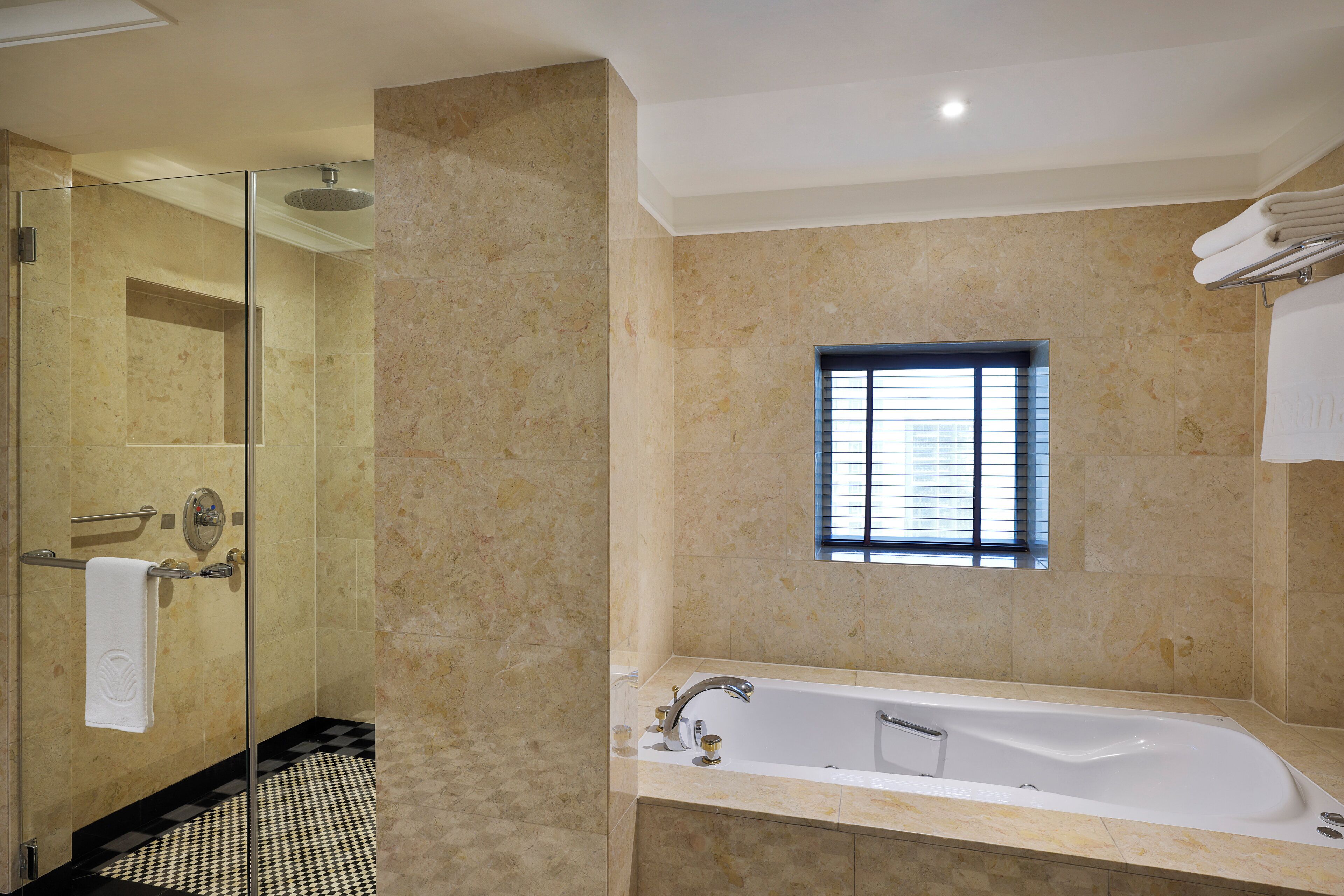 A modern bathroom with a glass-enclosed shower, a large bathtub, and a small window providing natural light.