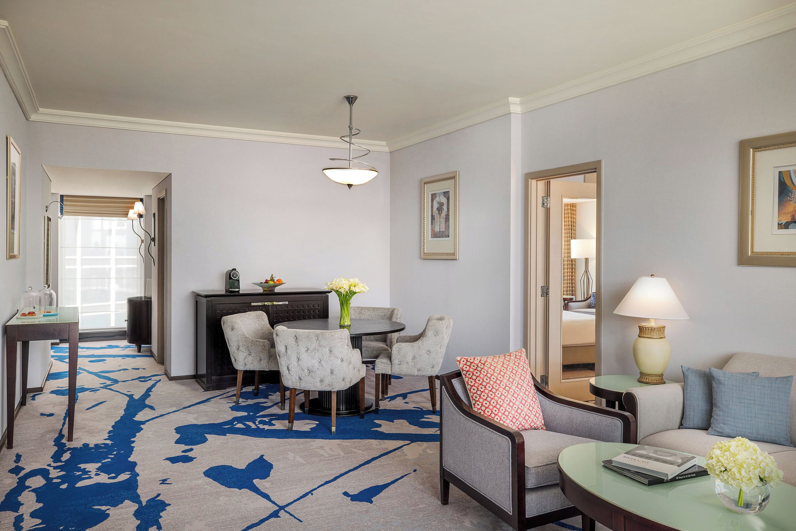 A hotel room with a dining area, a sofa, a coffee table, and a lamp.