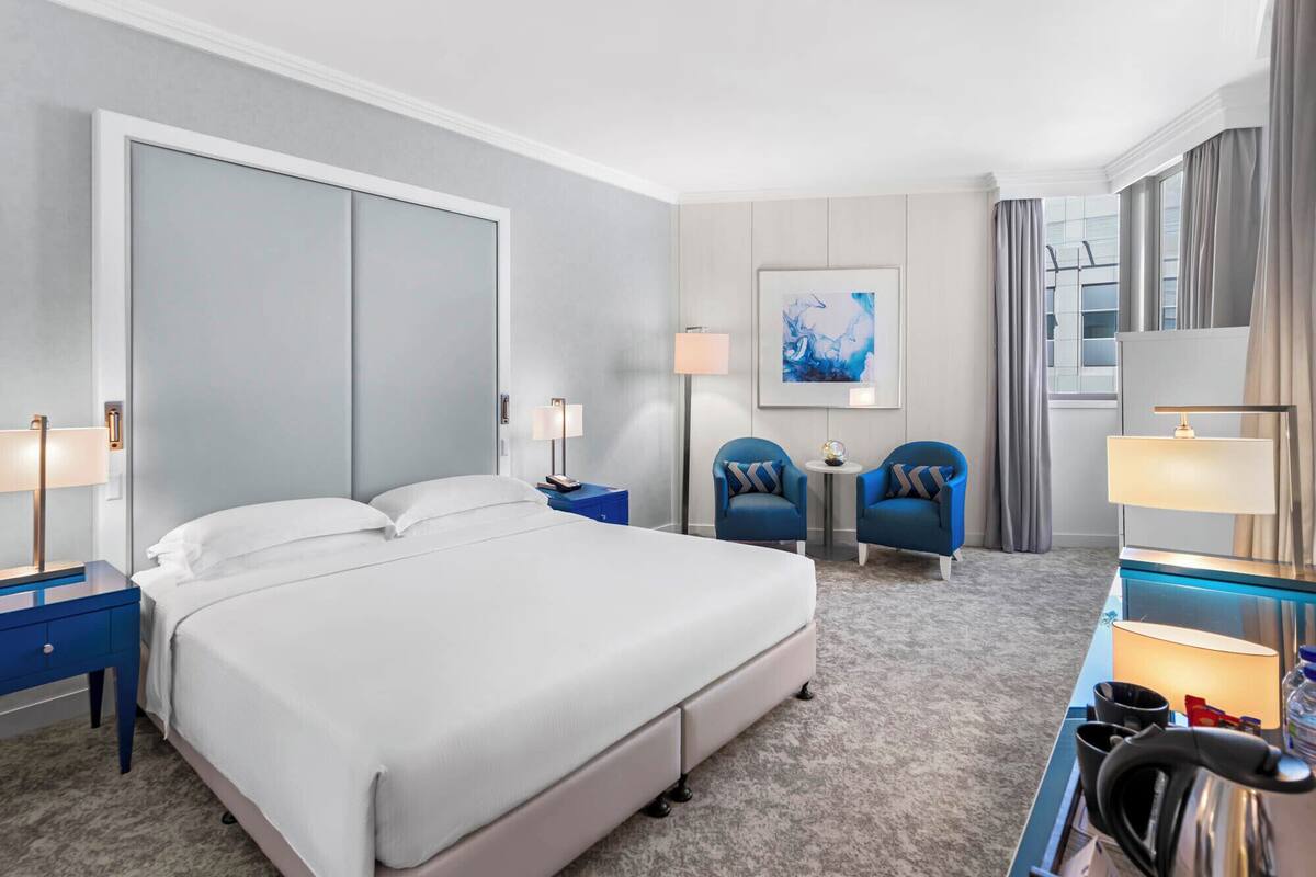 A hotel room with a large bed, two armchairs, a desk with a lamp, and a painting on the wall.