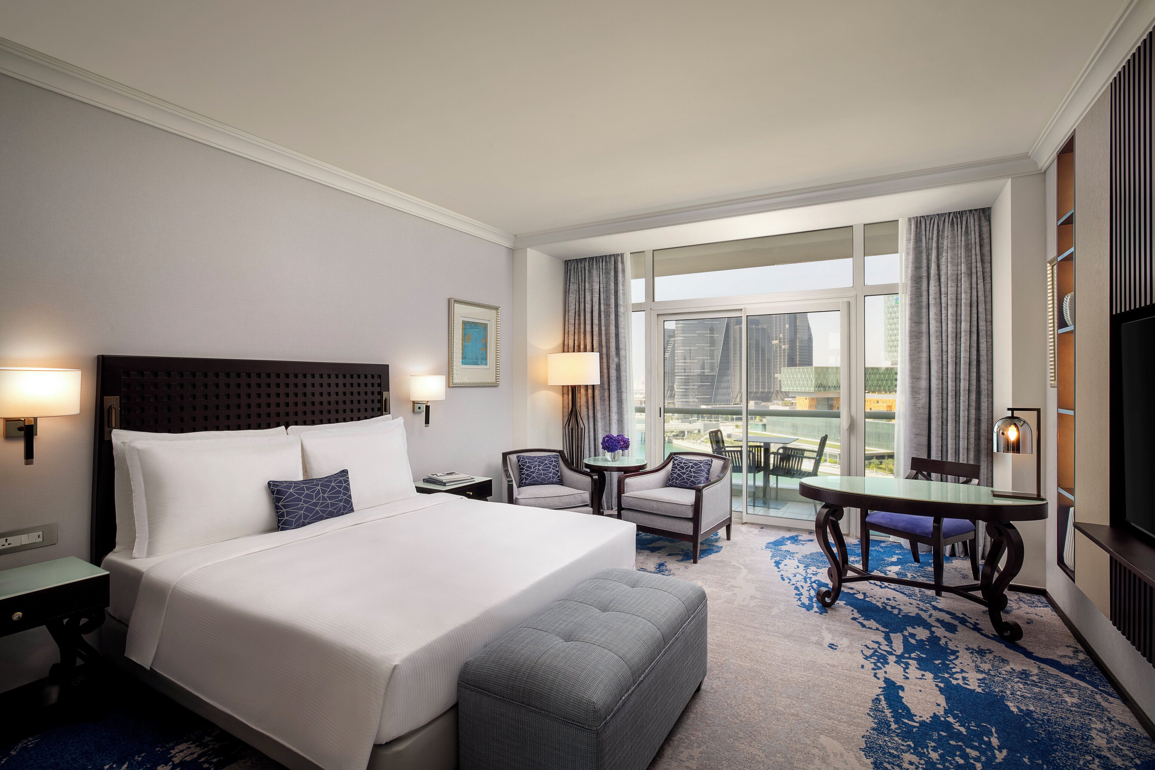 Ein Hotelzimmer mit einem großen Bett, zwei Sesseln, einem kleinen Tisch und einem Balkon mit Blick.