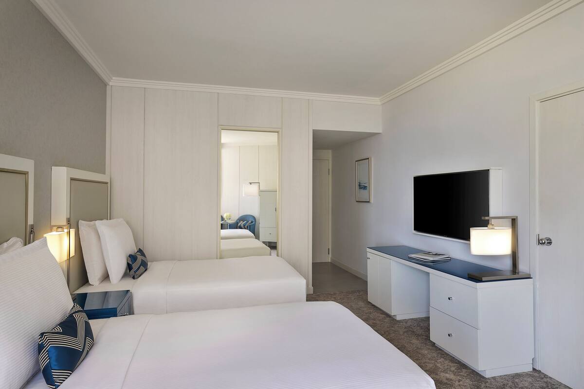 A hotel room with two beds, a desk with a flat-screen TV, a lamp, and a mirror.