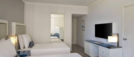 Habitación de hotel con dos camas, un escritorio, un televisor de pantalla plana, una lámpara y un espejo.