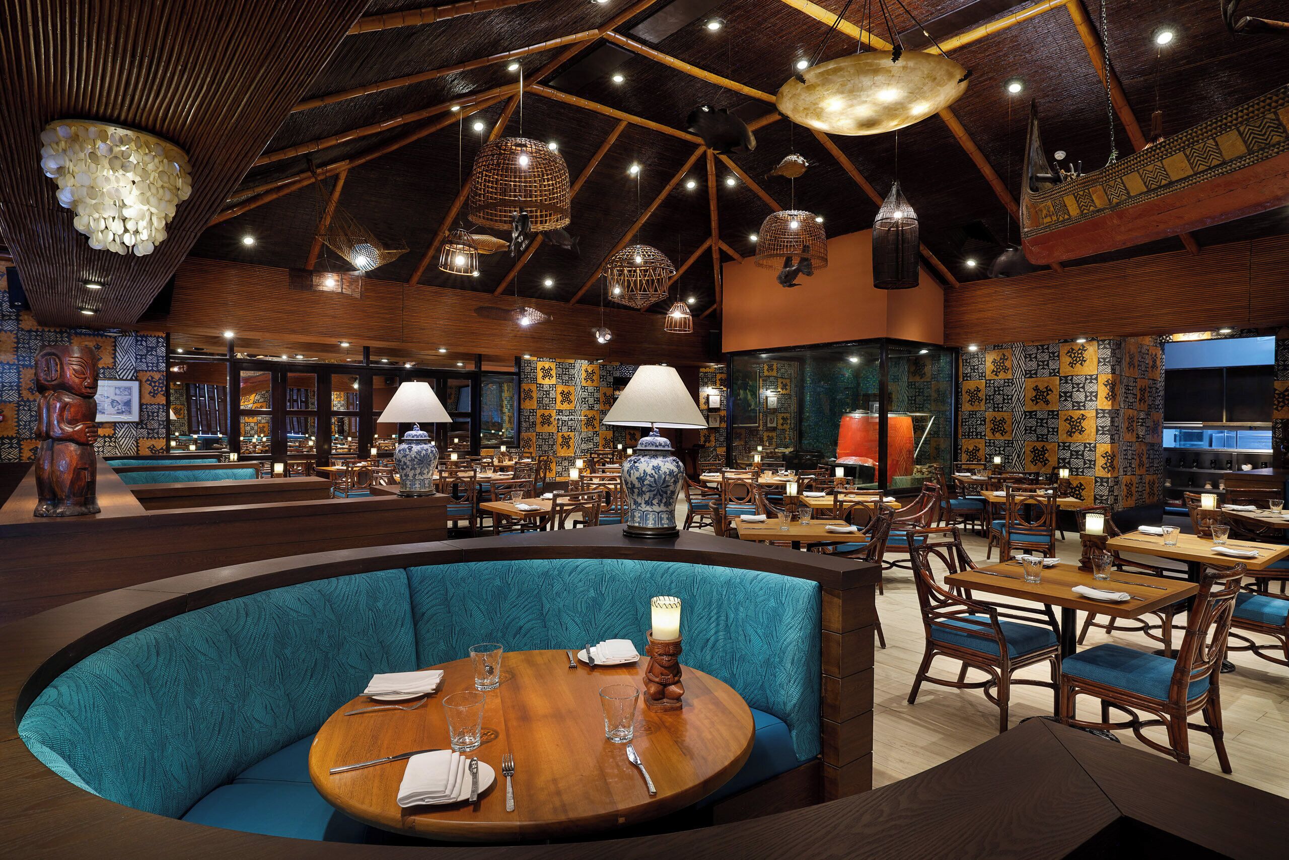 Un restaurant avec un plafond haut, des poutres en bois et des murs recouverts de carreaux décoratifs. On y trouve des tables et des banquettes avec un revêtement bleu.