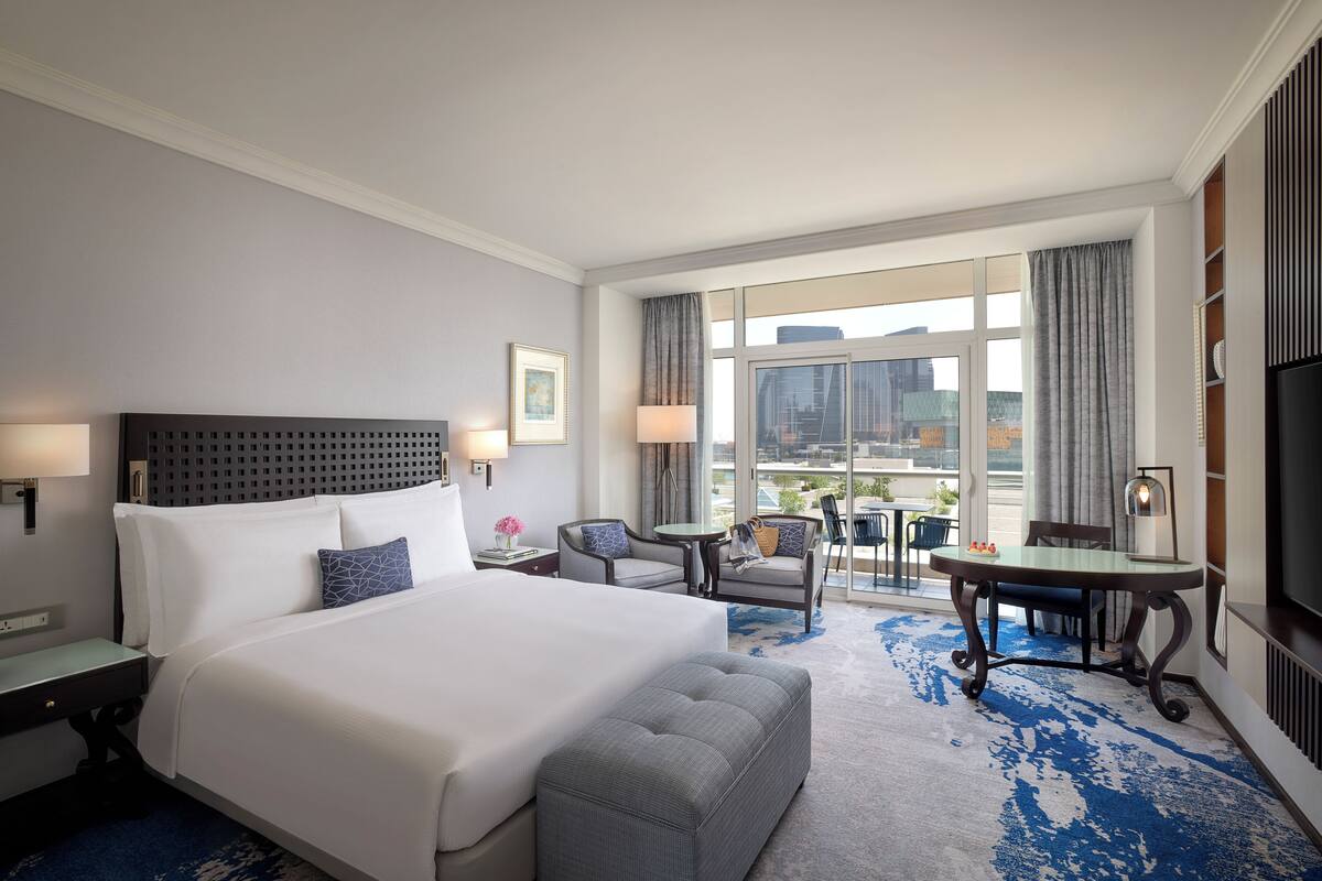 A hotel room with a large bed, a desk, a chair, a small table, and a TV.