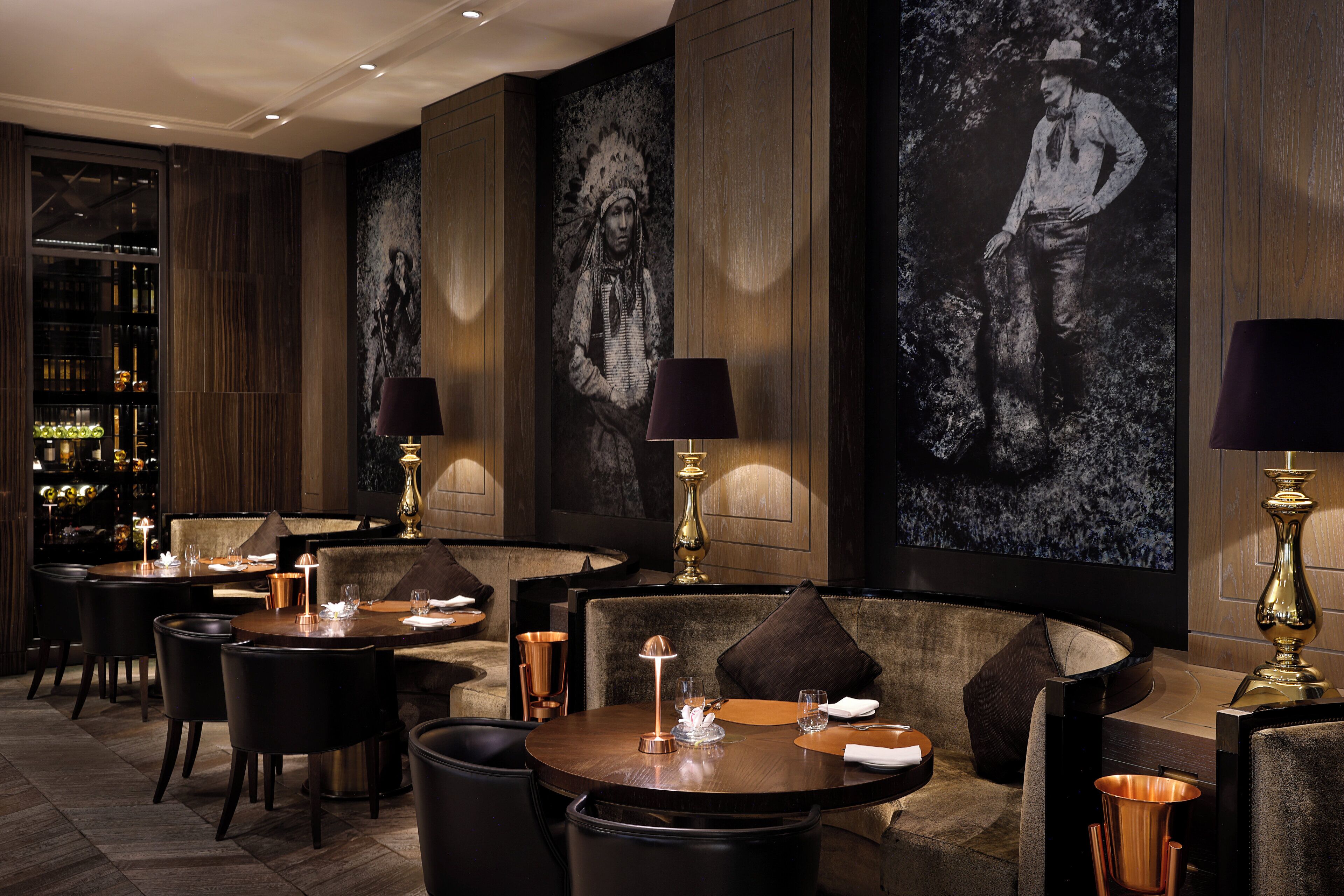 A restaurant with round tables, dark chairs, and a bar area with bottles.