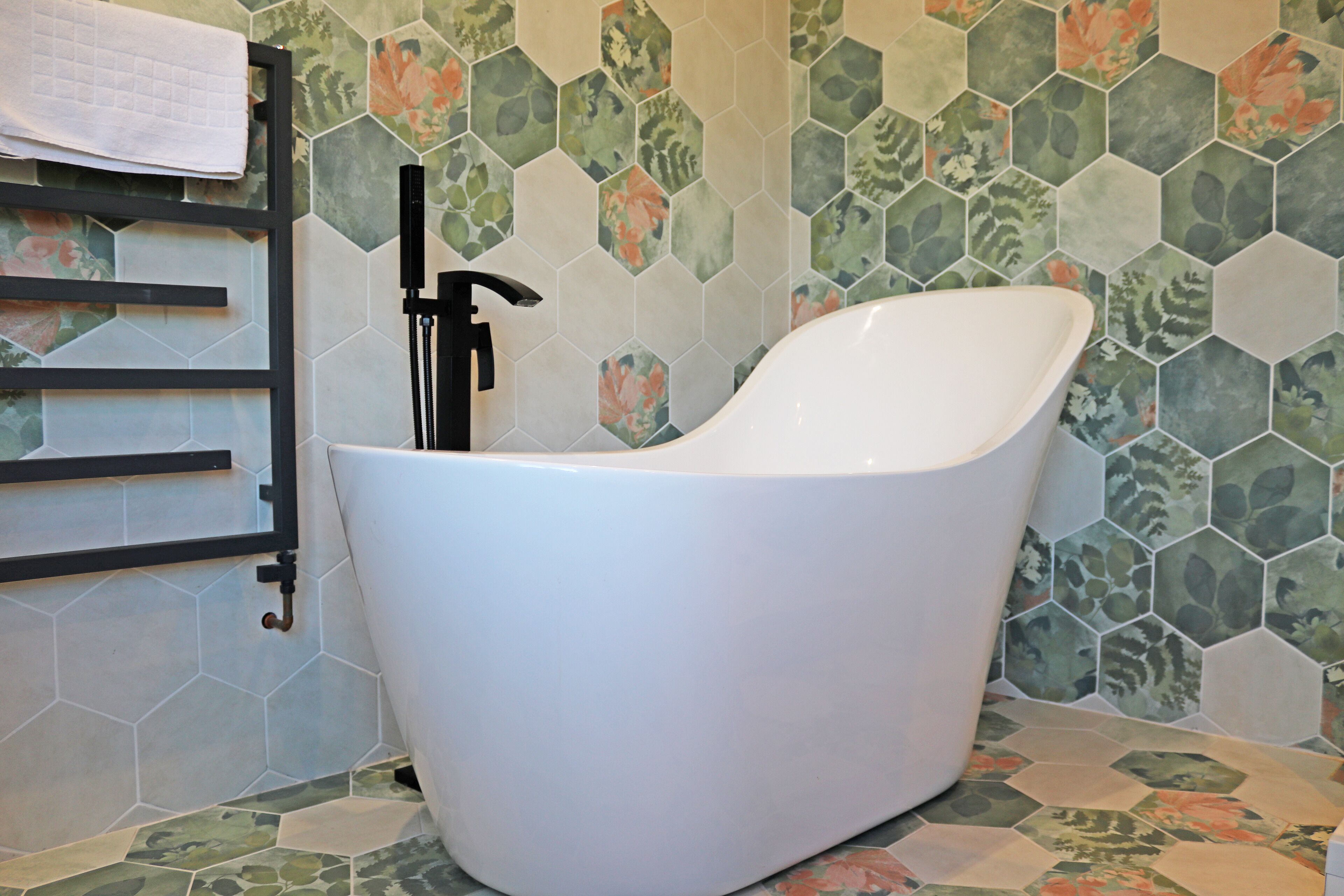 A modern bathroom with a freestanding bathtub, a towel rack, and a hexagonal tile backsplash.